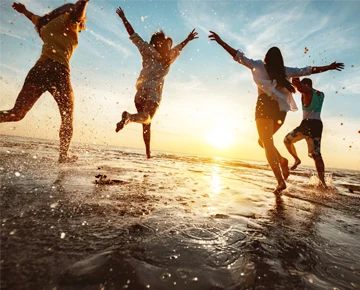 Personas saltando en la playa al atardecer